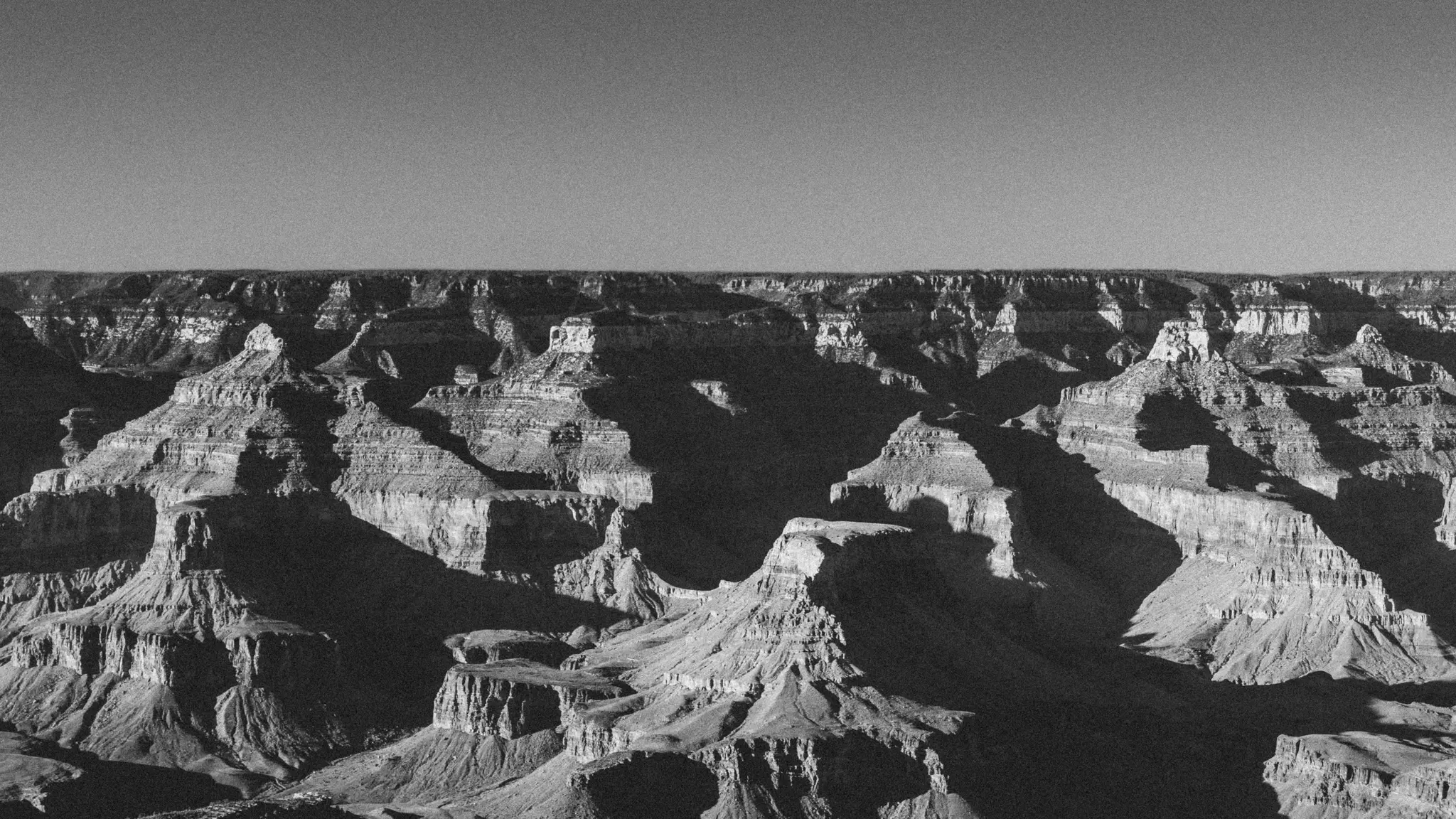 Vue panoramique en noir et blanc du Grand Canyon, montrant de nombreuses formations rocheuses superposées et des ombres