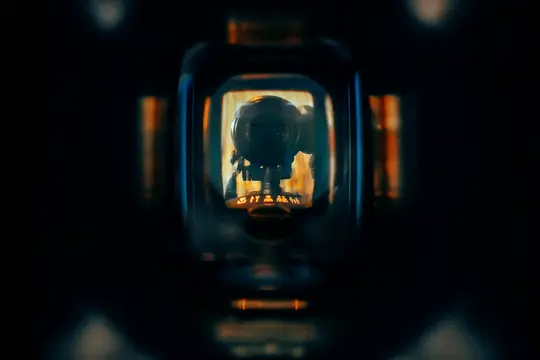 Tmavý záber zblízka kruhového zariadenia s hladkým, reflexným povrchom, zarámovaný obdĺžnikovým otvorom. Pod...