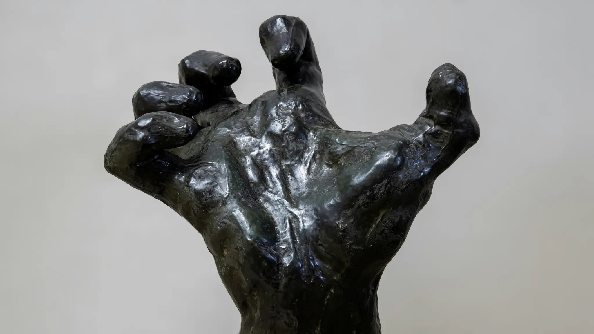 Une vue rapprochée, légèrement en angle, d'une sculpture en bronze sombre d'une main humaine. Les doigts sont recourbés vers