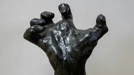 En nærbillede, let vinklet, af en mørk bronze skulptur af en menneskehånd. Fingrene er krøllet indad.