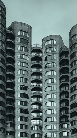 A low-angle, monochromatic photo of several brutalist concrete high-rise buildings. They feature rounded balconies and…