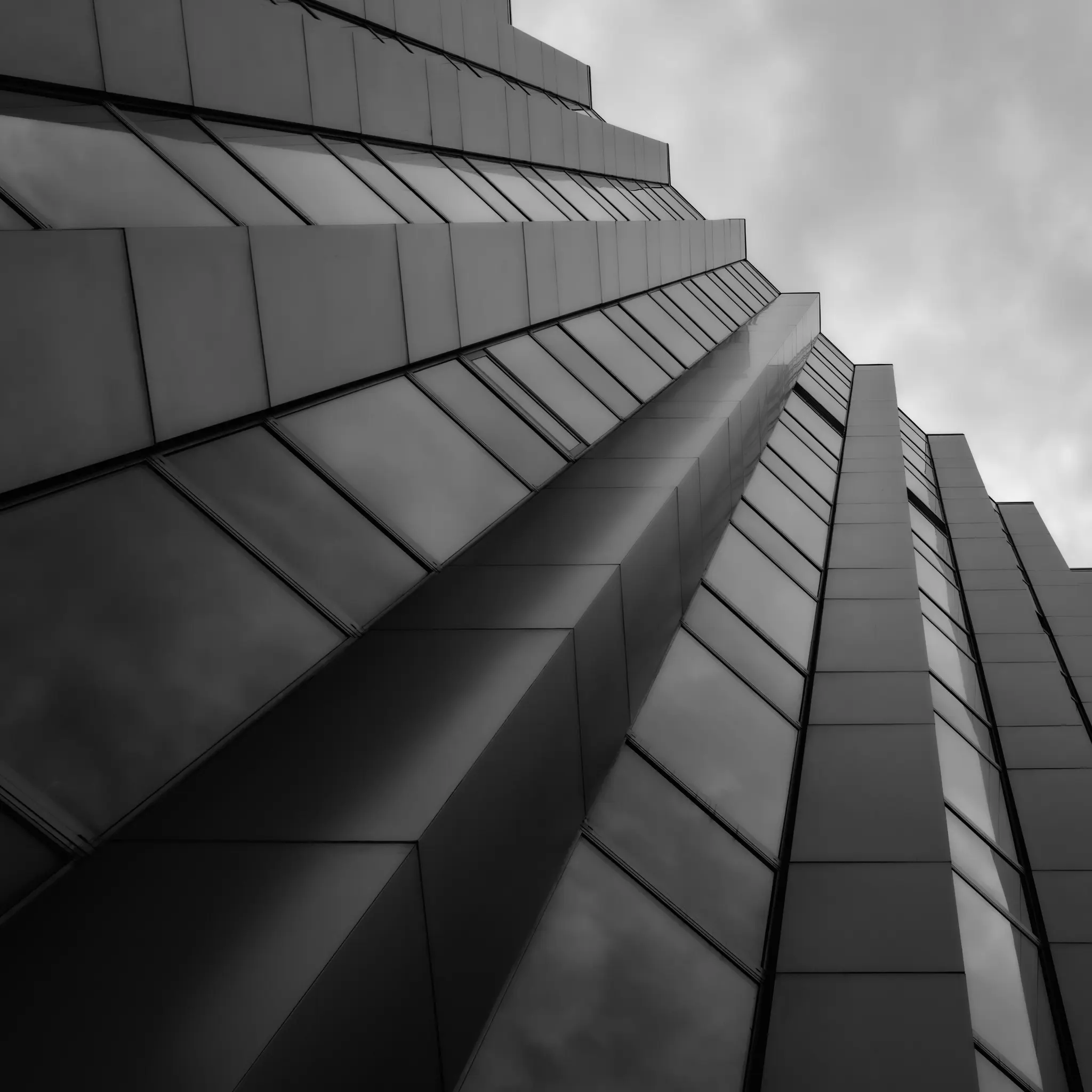Nízkoúhlý čiernobiely záber modernej fasády budovy s mnohými reflexnými oknami a tmavými geometrickými panelmi.