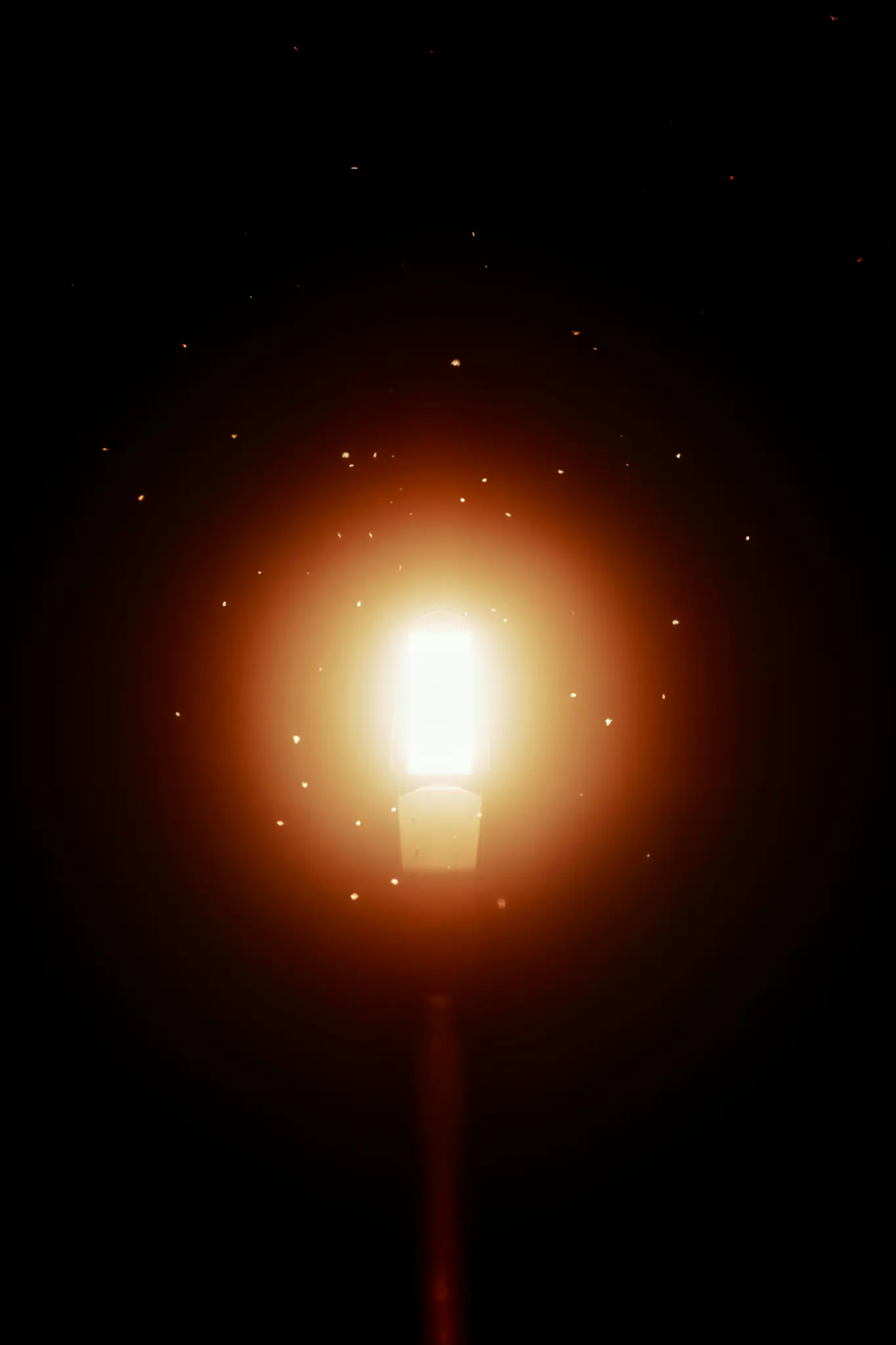 Un lampadaire lumineux et éclatant se détache sur un fond complètement sombre, entouré de nombreuses petites lumières