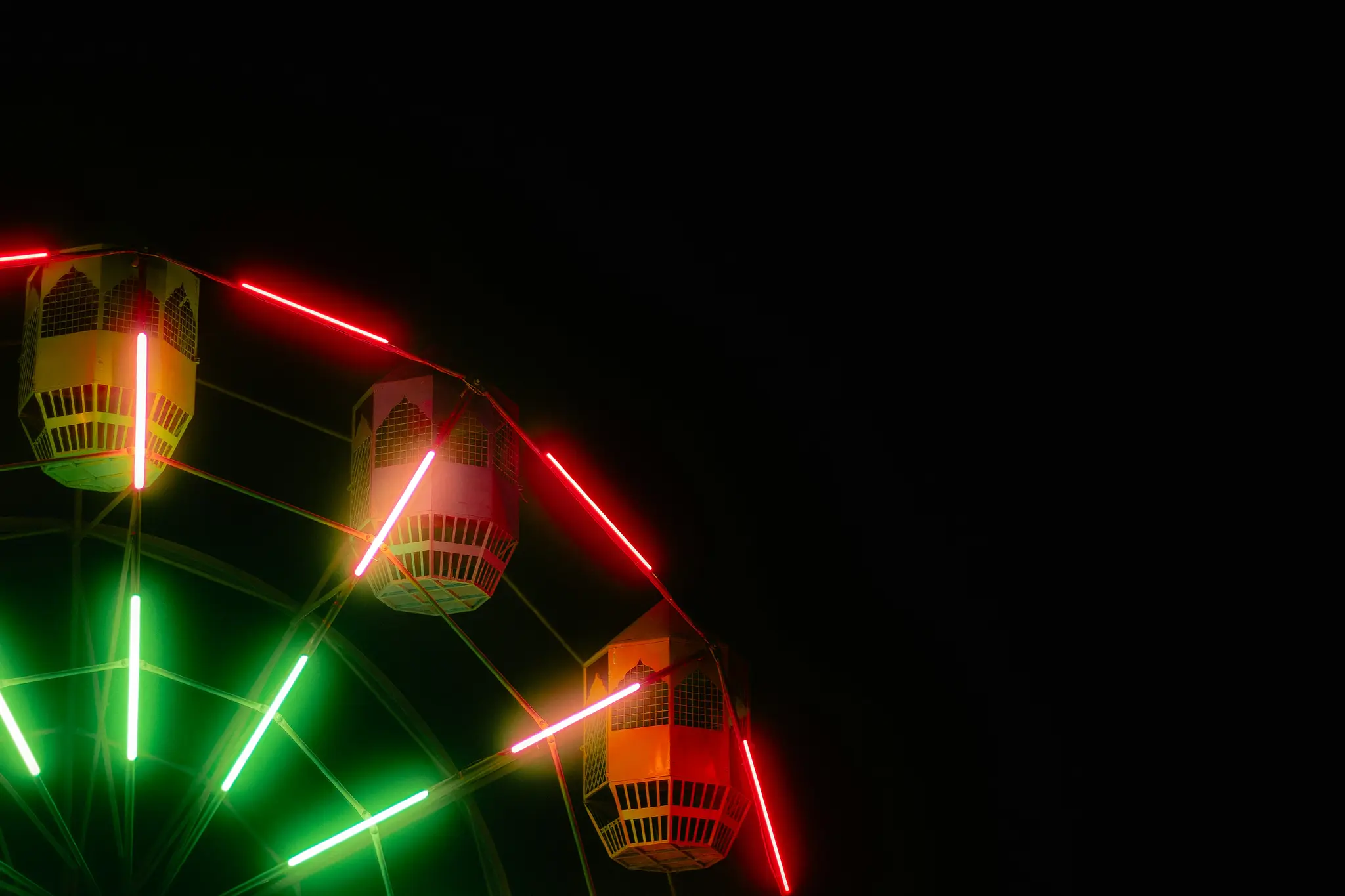 Une prise de vue rapprochée et dynamique d'une grande roue la nuit, avec des nacelles vivement éclairées et des néons rouges