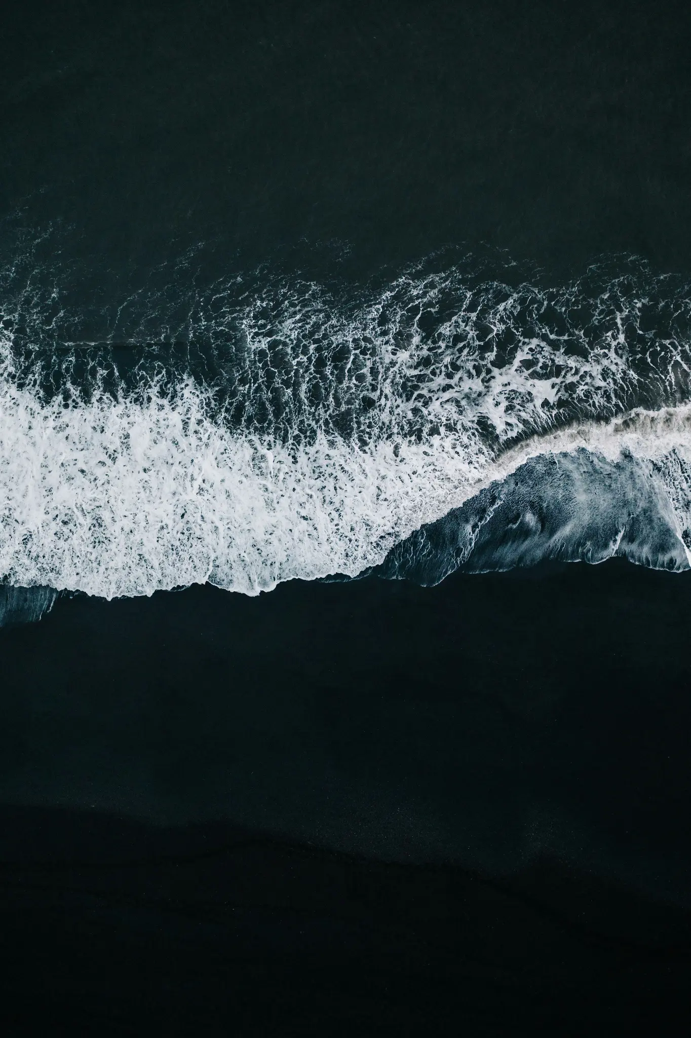 Una vista aerea, dall'alto, dell'oscura acqua dell'oceano con onde bianche e spumose che si infrangono su una spiaggia di