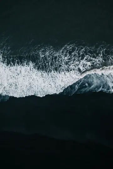 Una vista aerea, dall'alto, dell'oscura acqua dell'oceano con onde bianche e spumose che si infrangono su una spiaggia di