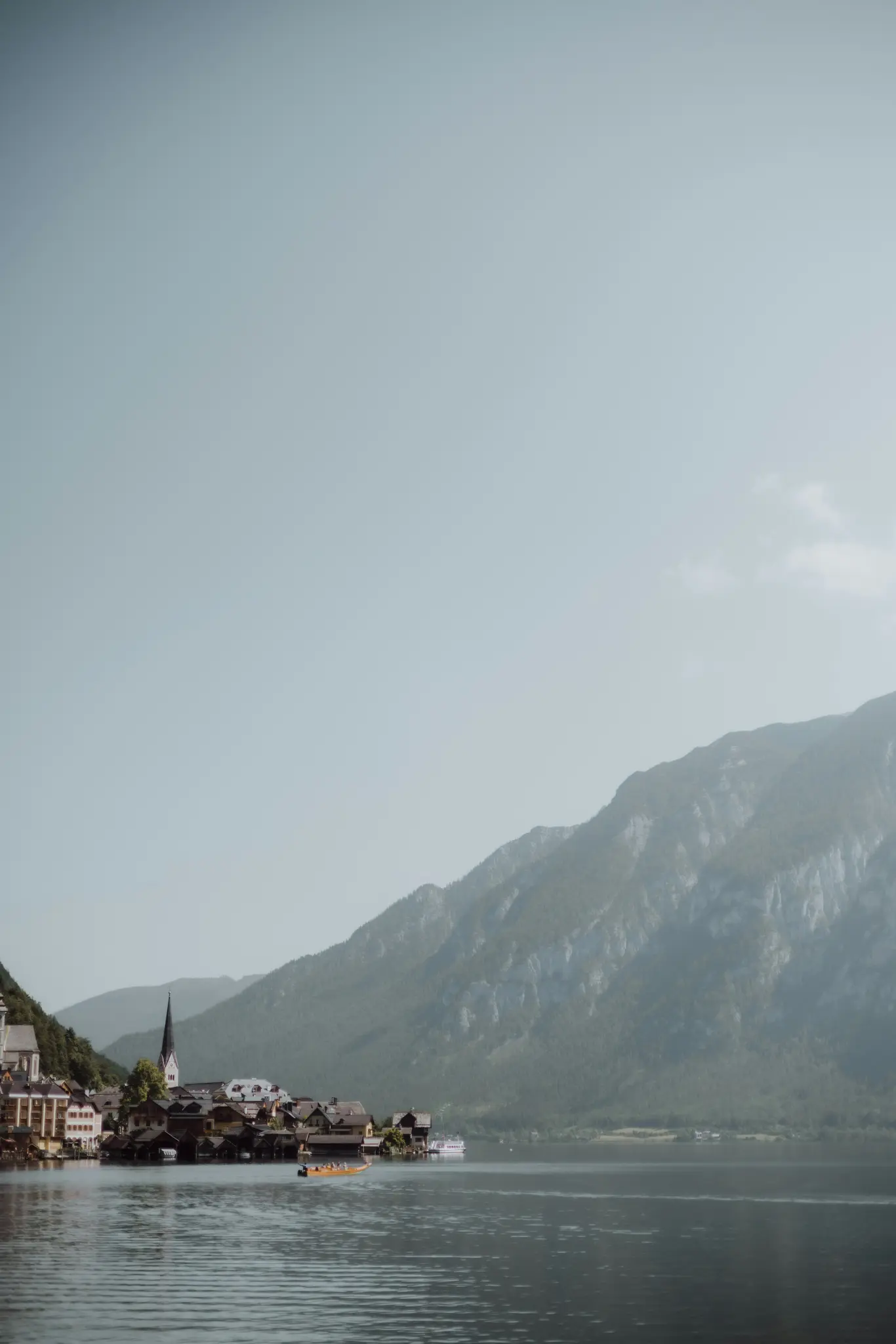 Eine weite Aufnahme eines malerischen Dorfes mit einer markanten Kirchturmspitze am Ufer eines ruhigen Sees, im Hintergrund