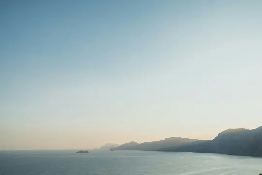 Un'ampia foto paesaggistica di una costa all'ora d'oro, che mostra montagne scure che incontrano un mare calmo sotto un cielo
