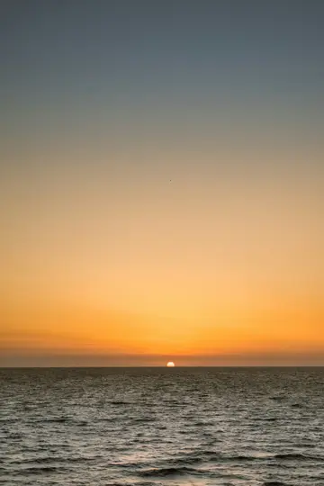 Ein lebendiger Sonnenuntergang über einer ruhigen Wasseroberfläche. Die Sonne, ein heller oranger Halbkreis, taucht knapp