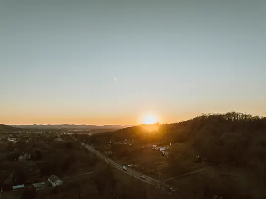 Eine Luftaufnahme eines Sonnenuntergangs über einer ländlichen Landschaft. Eine Straße mit Autos verläuft durch die Mitte