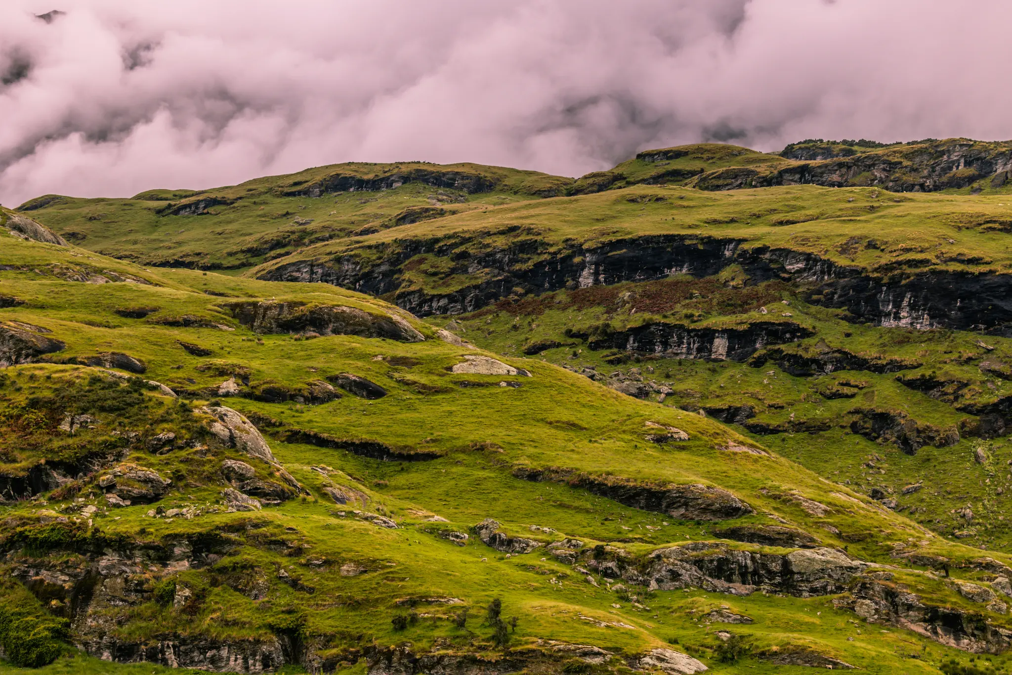 Un'ampia fotografia paesaggistica di lussureggianti colline verdi con affioramenti rocciosi e sporgenze visibili sotto un
