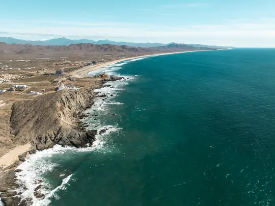 Una vista aerea cattura un lungo tratto di costa con una città, una spiaggia sabbiosa e scogliere rocciose che incontrano