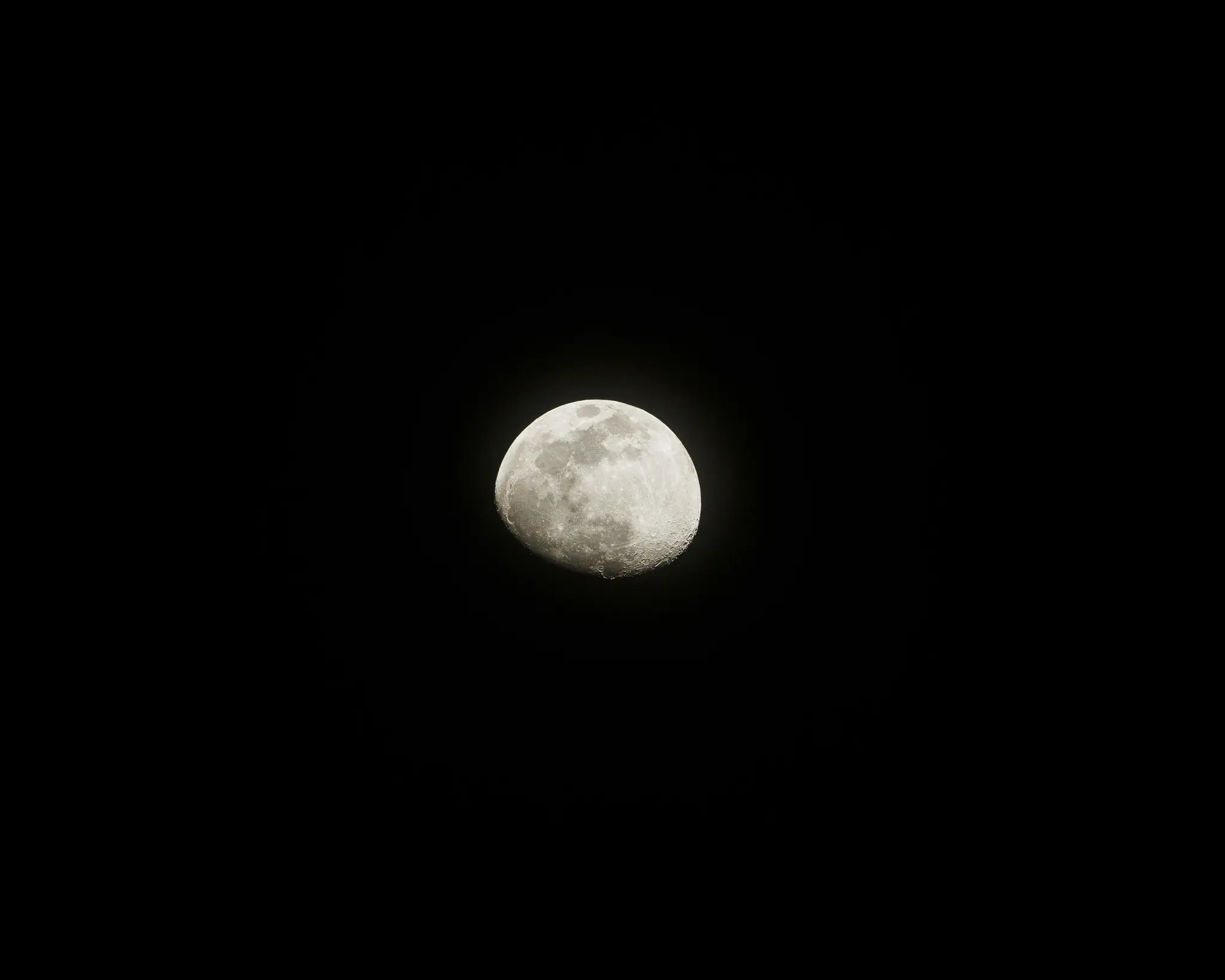 Een gedetailleerd beeld van een gibbous maan, fel verlicht en met kraters en schaduwen, tegen een volledig zwarte hemel.