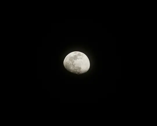 Eine detaillierte Ansicht eines Halbmonds, hell beleuchtet und mit Kratern und Schatten, vor einem komplett schwarzen Himmel.