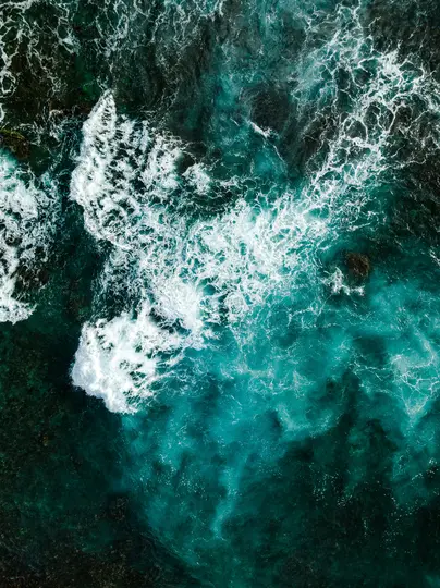 Una vista aerea, dall'alto, dell'acqua dell'oceano. Onde bianche e spumose si infrangono sulla superficie di acqua verde