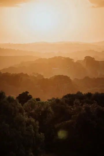 Ein verschwommenes, warm getöntes Landschaftsfoto, das mehrere Schichten von bewaldeten Hügeln unter einer hellen, weichen