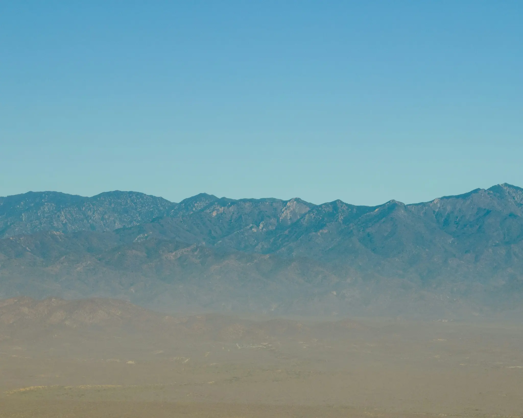 Breite Landschaftsaufnahme, die eine entfernte Bergkette mit zerklüfteten Gipfeln unter einem klaren, strahlend blauen Himmel