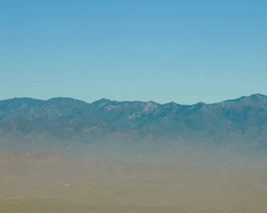 Breite Landschaftsaufnahme, die eine entfernte Bergkette mit zerklüfteten Gipfeln unter einem klaren, strahlend blauen Himmel