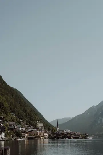 Una ripresa ampia del villaggio di Hallstatt con edifici tradizionali e un campanile, situato su un lago con montagne.