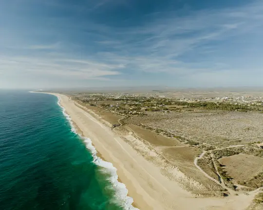 Uno scatto aereo mostra una vasta spiaggia sabbiosa che si snoda lungo un oceano turchese, con onde bianche che si