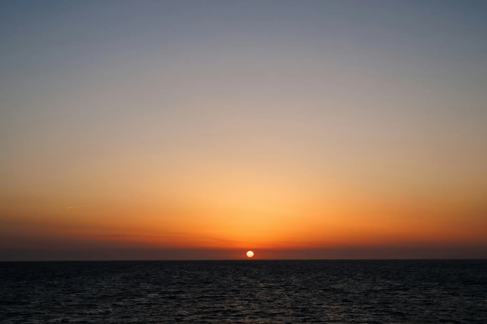 Un vibrante tramonto su una distesa d'acqua calma. Il sole, un globo arancione brillante, si trova appena sopra la linea