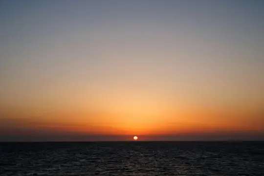 Ein lebendiger Sonnenuntergang über einem ruhigen Gewässer. Die Sonne, eine leuchtend orangefarbene Kugel, befindet sich