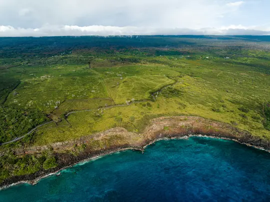 Una fotografia aerea mostra un vibrante paesaggio verde che incontra una costa frastagliata, con scogliere che scendono in un