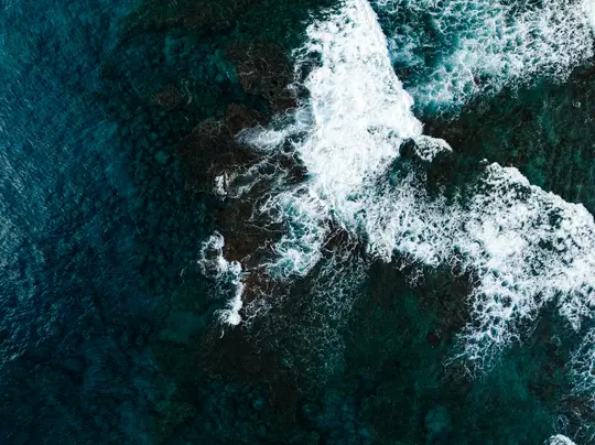 Uno scatto aereo cattura acqua oceanica di un profondo blu turchese con onde bianche e spumeggianti che si infrangono su