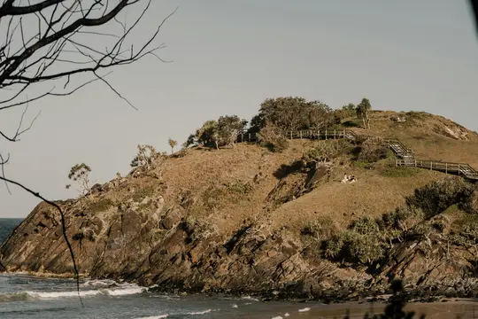 Un'ampia foto paesaggistica di un promontorio costiero roccioso coperto di erba secca e alberi sparsi, con l'oceano alla sua