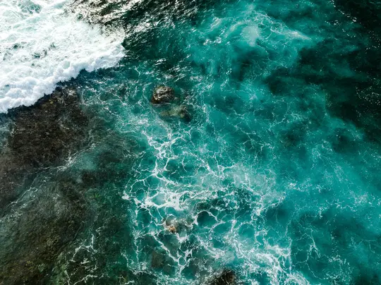 Una ripresa aerea mostra vibranti acque oceaniche turchesi e acquamarina con onde bianche e spumeggianti che si infrangono su