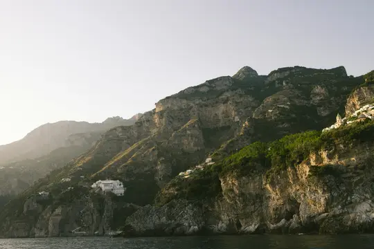 Eine malerische Aussicht auf raue, grüne und braune Berge, die steil aus dunkelblauem Wasser unter einem blassen Himmel