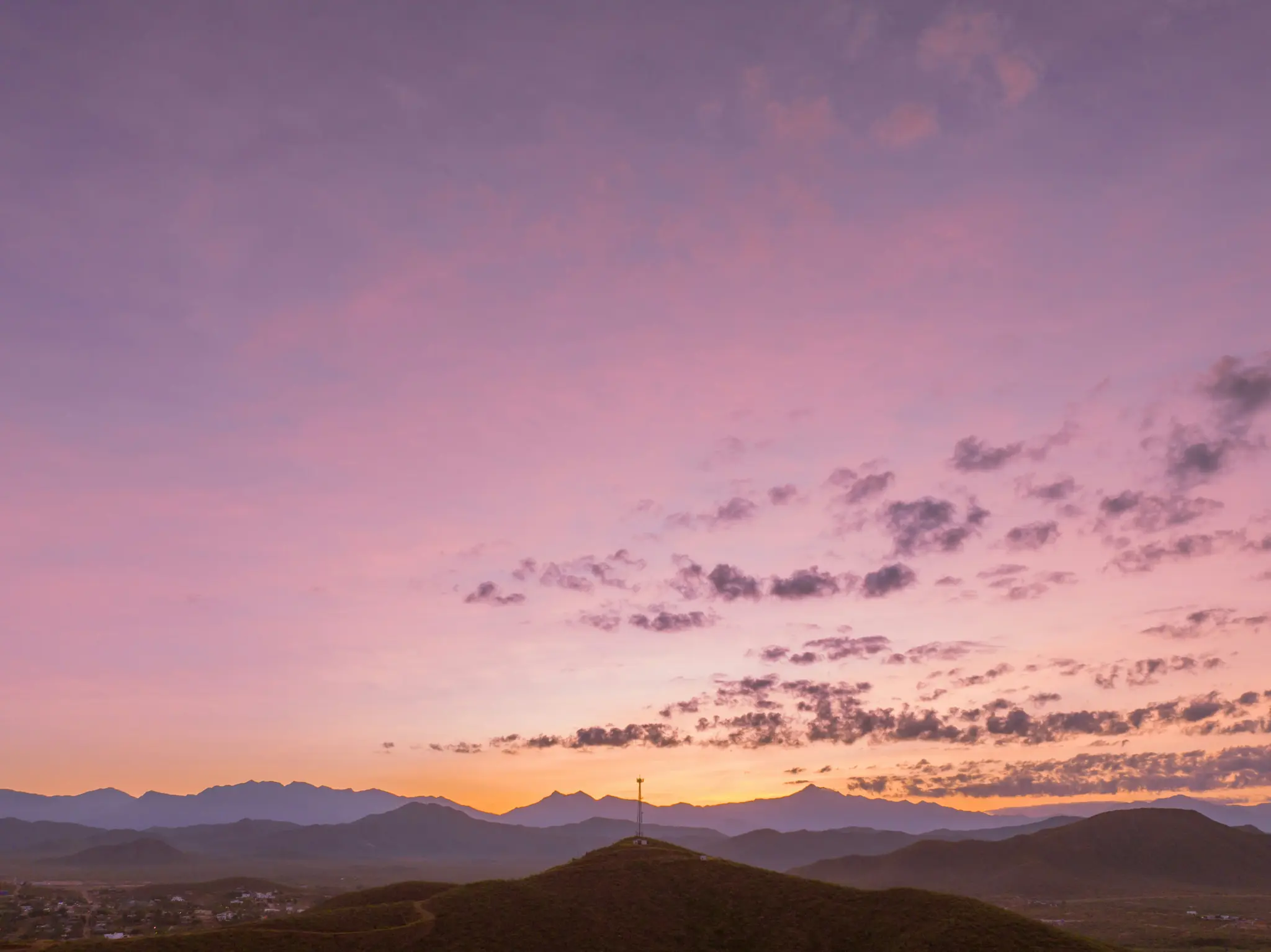 Un vibrante tramonto dipinge il cielo con sfumature viola, rosa e arancioni su una catena montuosa. Una torre di