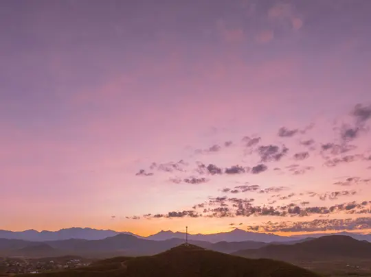 Un vibrante tramonto dipinge il cielo con sfumature viola, rosa e arancioni su una catena montuosa. Una torre di