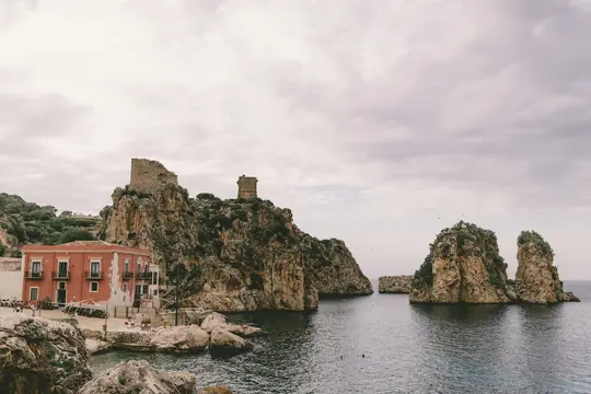 Un edificio rosso si trova vicino a una costa rocciosa con antiche torri di pietra su scogliere e diversi faraglioni nel