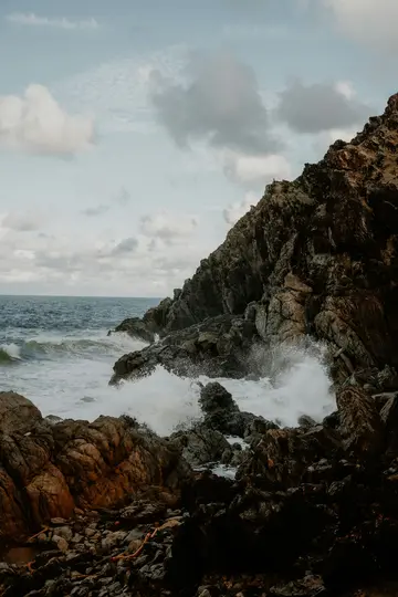 Una drammatica foto di paesaggio di grandi onde che si infrangono su rocce scure e frastagliate in una giornata nuvolosa, con