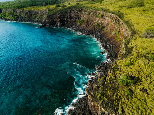Uno scatto aereo di una drammatica costa dove una ripida scogliera verde incontra il vibrante oceano turchese.