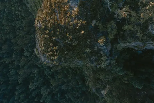An aerial, top-down view of a rugged, brown rocky outcrop covered in sparse, light green vegetation, surrounded by a dark…