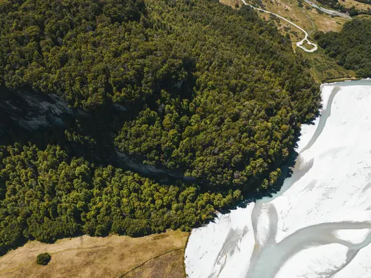 Uno scatto aereo cattura una lussureggiante foresta verde sulla sinistra, che incontra un ampio letto di fiume intrecciato di