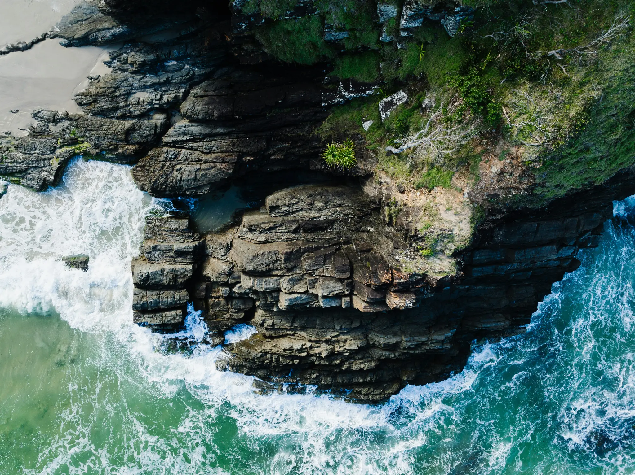 Une vue aérienne, de haut en bas, d'une côte accidentée où des falaises verdoyantes rencontrent l'océan, avec des vagues