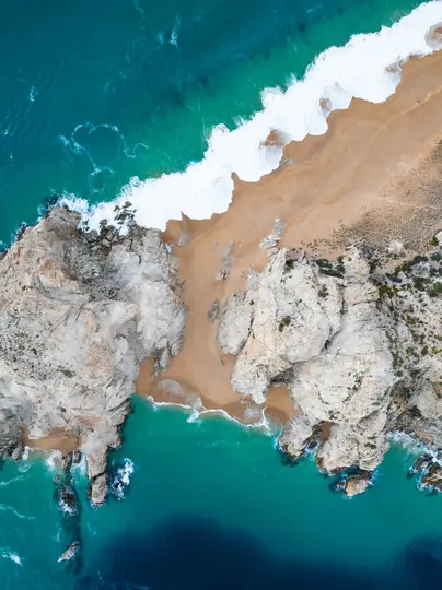 Uno scatto aereo mostra una spiaggia sabbiosa incastonata tra scogliere rocciose chiare e vibranti acque oceaniche turchesi.
