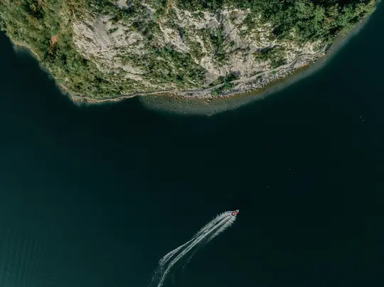 Uno scatto aereo cattura una piccola barca rossa e bianca che solca l'acqua blu scuro, lasciando una scia bianca distintiva.