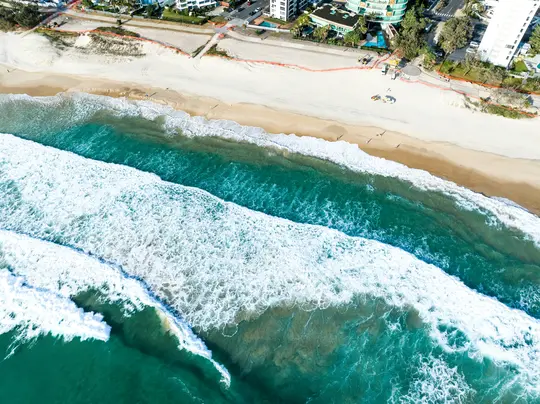 Una fotografia aerea cattura onde turchesi dell'oceano con schiuma bianca che si infrangono su un'ampia spiaggia sabbiosa