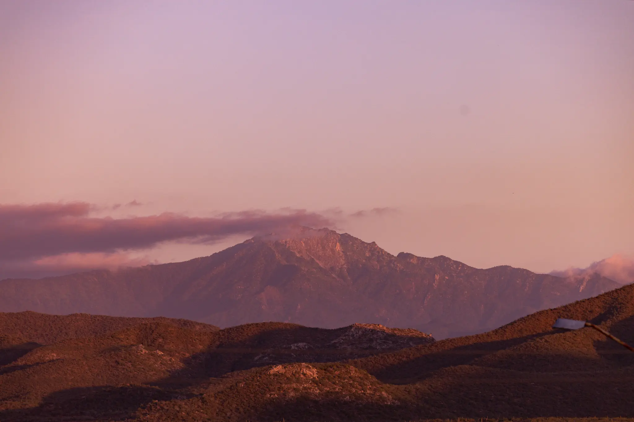 Un'ampia foto panoramica di una catena montuosa e dolci colline sotto un cielo rosa e viola durante l'ora d'oro. Le nuvole