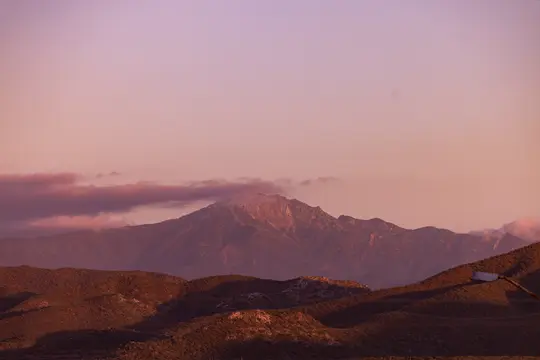 Breite Landschaftsaufnahme einer Bergkette und sanfter Hügel unter einem rosa und violetten Himmel während der goldenen