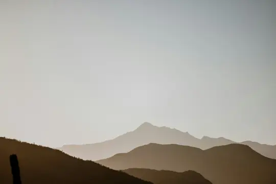 Una foto minimalista di paesaggio che mostra più strati di silhouette di montagne e colline marrone scuro su uno sfondo di