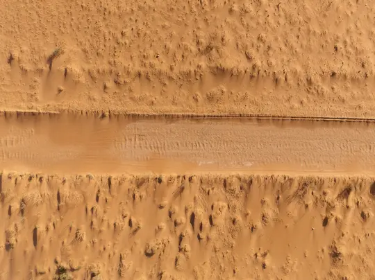 Una vista aerea, dall'alto verso il basso, di un paesaggio desertico. Una pista sabbiosa più chiara attraversa