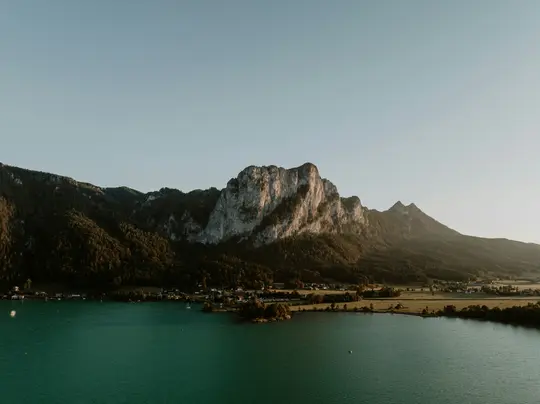 Eine weite Aufnahme eines teal-farbenen Sees, der das goldene Licht der untergehenden Sonne reflektiert, mit einer großen