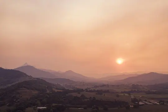 Una foto aerea del paesaggio che mostra strati di montagne e colline sotto un cielo arancione nebbioso con il sole che brilla