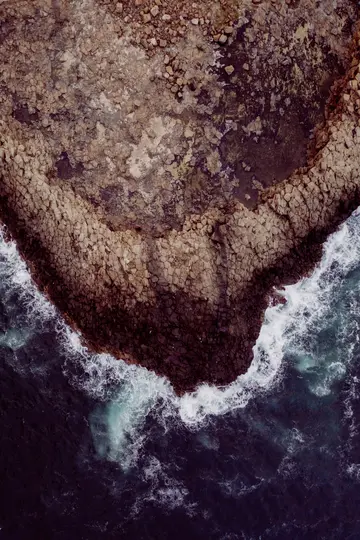 Una vista aerea, dall'alto, di una costa frastagliata dove le onde dell'oceano blu scuro con schiuma bianca si infrangono