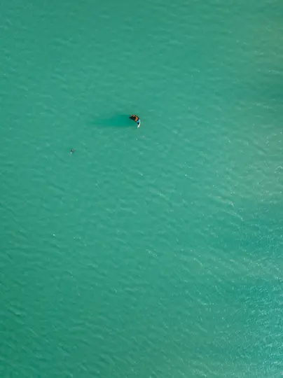 Eine Luftaufnahme eines einzelnen Kitesurfers auf einer weiten, schimmernden türkisfarbenen Wasserfläche bei hellem